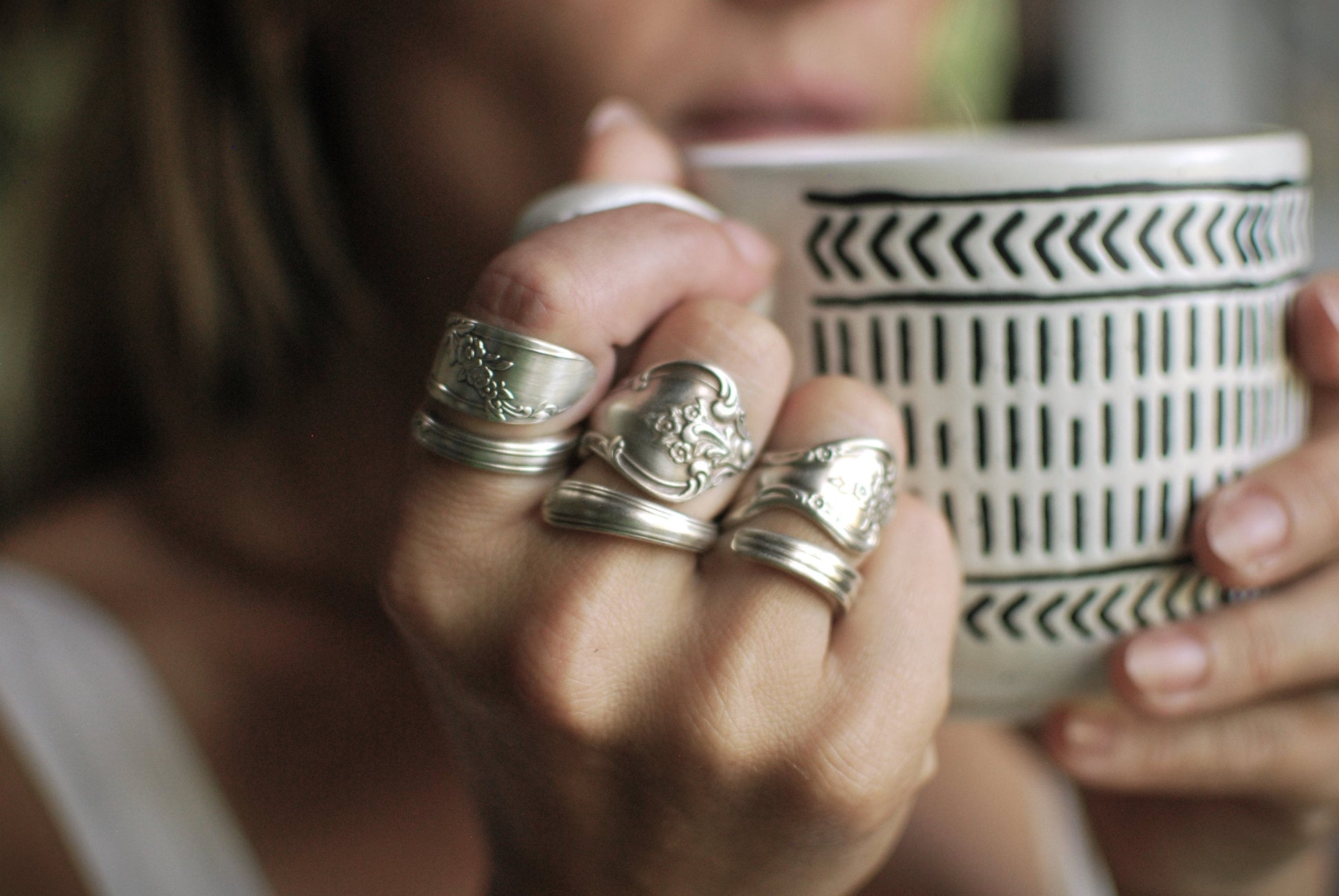 May include: Five silver spoon rings stacked on a finger.